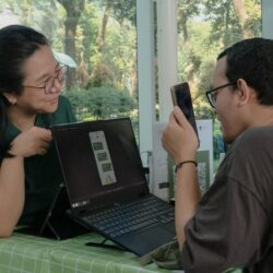 Man scanning laptop screen with phone, woman watching