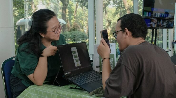 Man scanning laptop screen with phone, woman watching