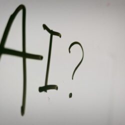 The letters AI and a question mark written in black marker on a whiteboard