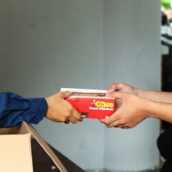 A person handing a box of pizza to another person