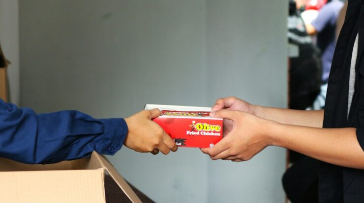 A person handing a box of pizza to another person