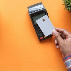 A person holding a blank credit card near a payment terminal on orange