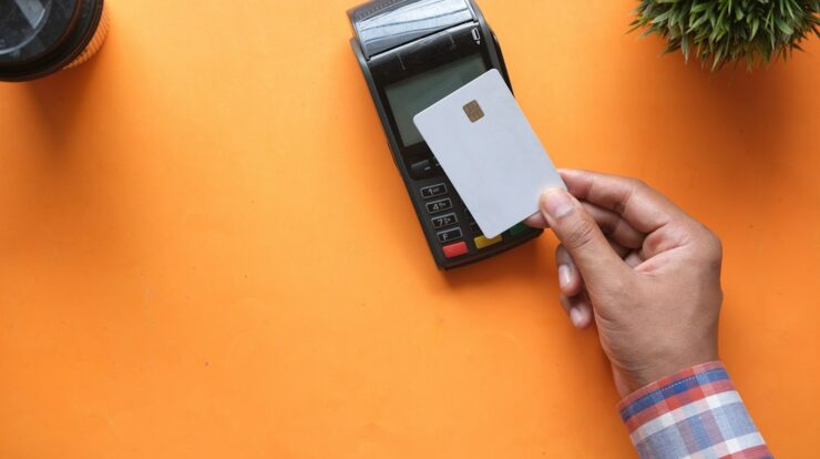 A person holding a blank credit card near a payment terminal on orange