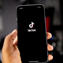 A hand holding a smartphone displaying the TikTok logo on a black screen