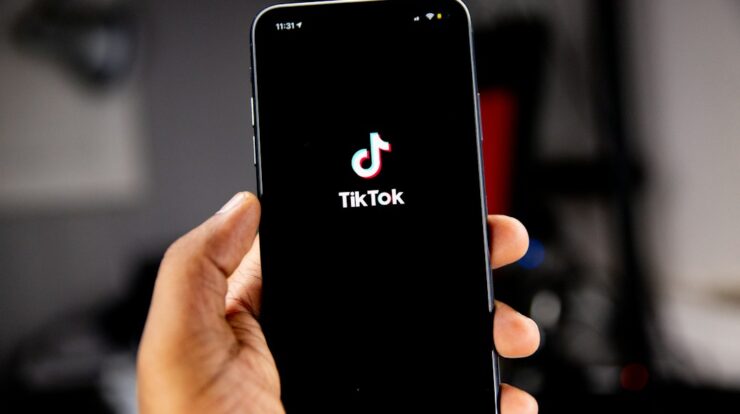 A hand holding a smartphone displaying the TikTok logo on a black screen