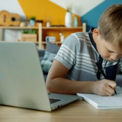 Young boy studies at a laptop and notebook
