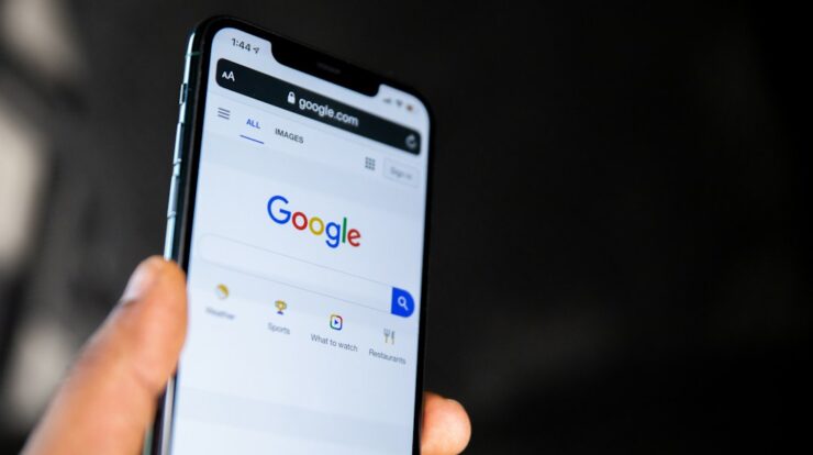 A hand holding a smartphone displaying the Google search engine homepage