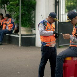 Two traffic officers in orange vests check their phones