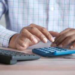 person using calculator at desk with coffee mug