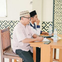 Two men wearing kufi caps attend a meeting