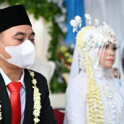 a man wearing a face mask sitting next to a woman in a wedding dress