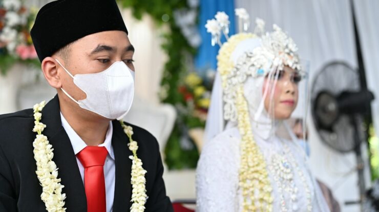 a man wearing a face mask sitting next to a woman in a wedding dress