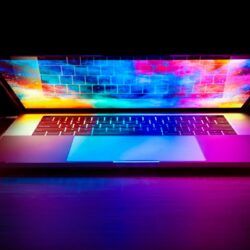 A laptop with a vibrant colorful screen glowing on a dark wooden desk