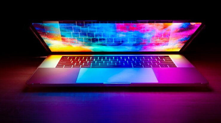 A laptop with a vibrant colorful screen glowing on a dark wooden desk