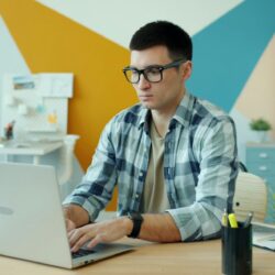 Man wearing glasses typing on laptop at desk