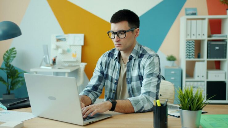 Man wearing glasses typing on laptop at desk