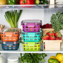 Colorful plastic food containers stacked inside a refrigerator with fresh produce