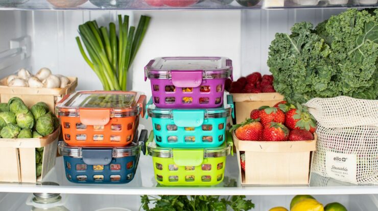 Colorful plastic food containers stacked inside a refrigerator with fresh produce