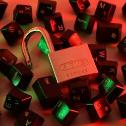 An open padlock surrounded by scattered black computer keyboard keys under red and green light