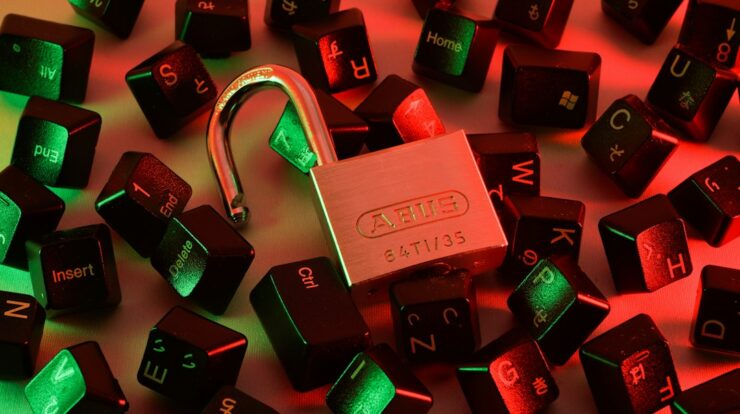 An open padlock surrounded by scattered black computer keyboard keys under red and green light